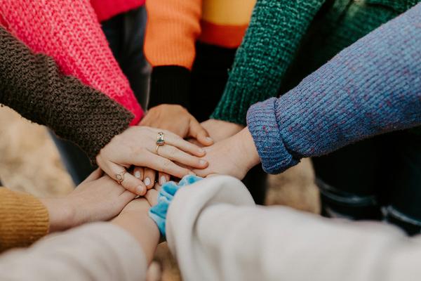People in colourful sweaters are holding hands as a gesture of collaboration and support. 